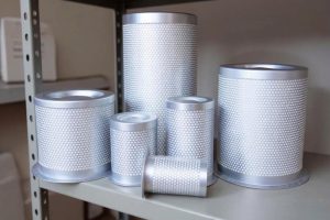 Bộ sưu tập các loại lọc tách dầu máy nén khí trục vít với kích thước khác nhau, vỏ kim loại đục lỗ lưới tổ ong và có khói bốc lên mô phỏng hiệu suất lọc hơi dầu