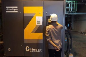 Kỹ thuật viên đang kiểm tra máy nén khí không dầu Atlas Copco Z series, nổi bật với dòng chữ "Oil-free air" chứng nhận khí sạch 100% phù hợp cho y tế và thực phẩm.