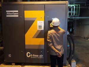 Kỹ thuật viên đang kiểm tra máy nén khí không dầu Atlas Copco Z series, nổi bật với dòng chữ "Oil-free air" chứng nhận khí sạch 100% phù hợp cho y tế và thực phẩm.